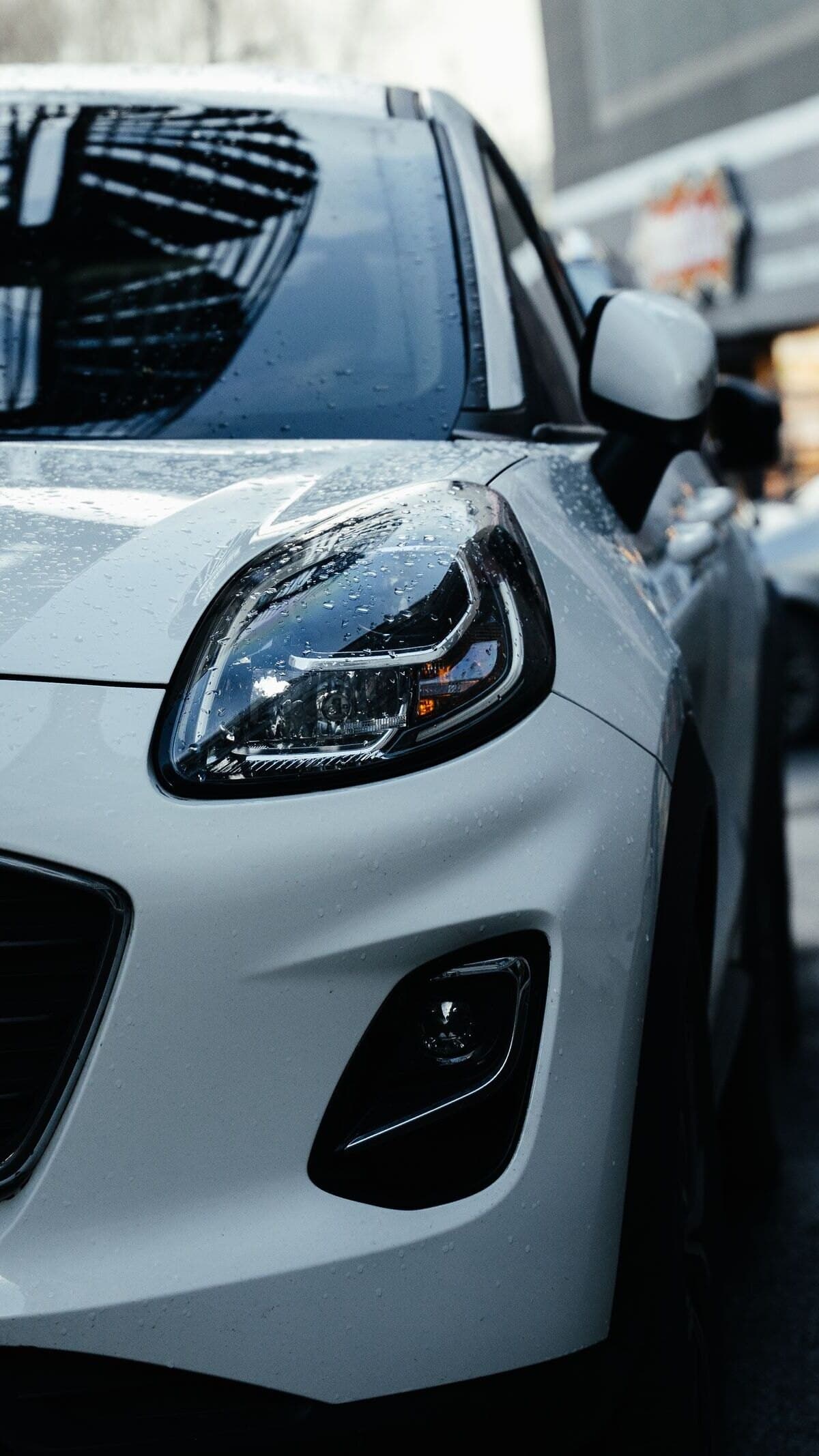 Front of a white Ford Puma on a rain-soaked street