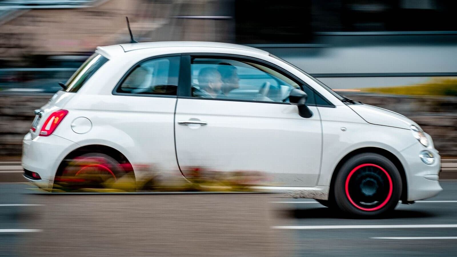 A white Fiat 500 driving through a Maltese town